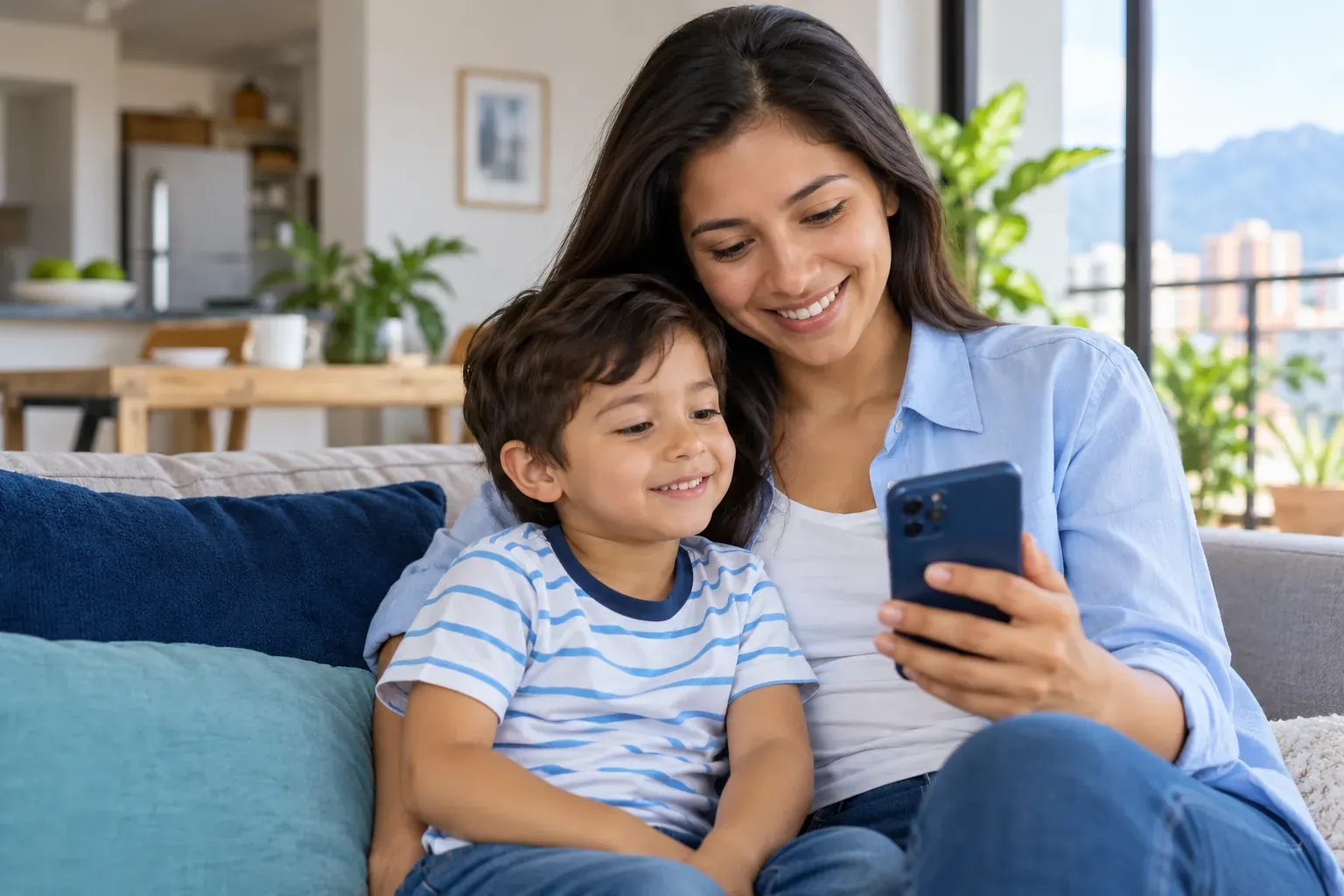 Madre y su hijo pequeño sonriendo mientras miran juntos el celular en la sala de su casa